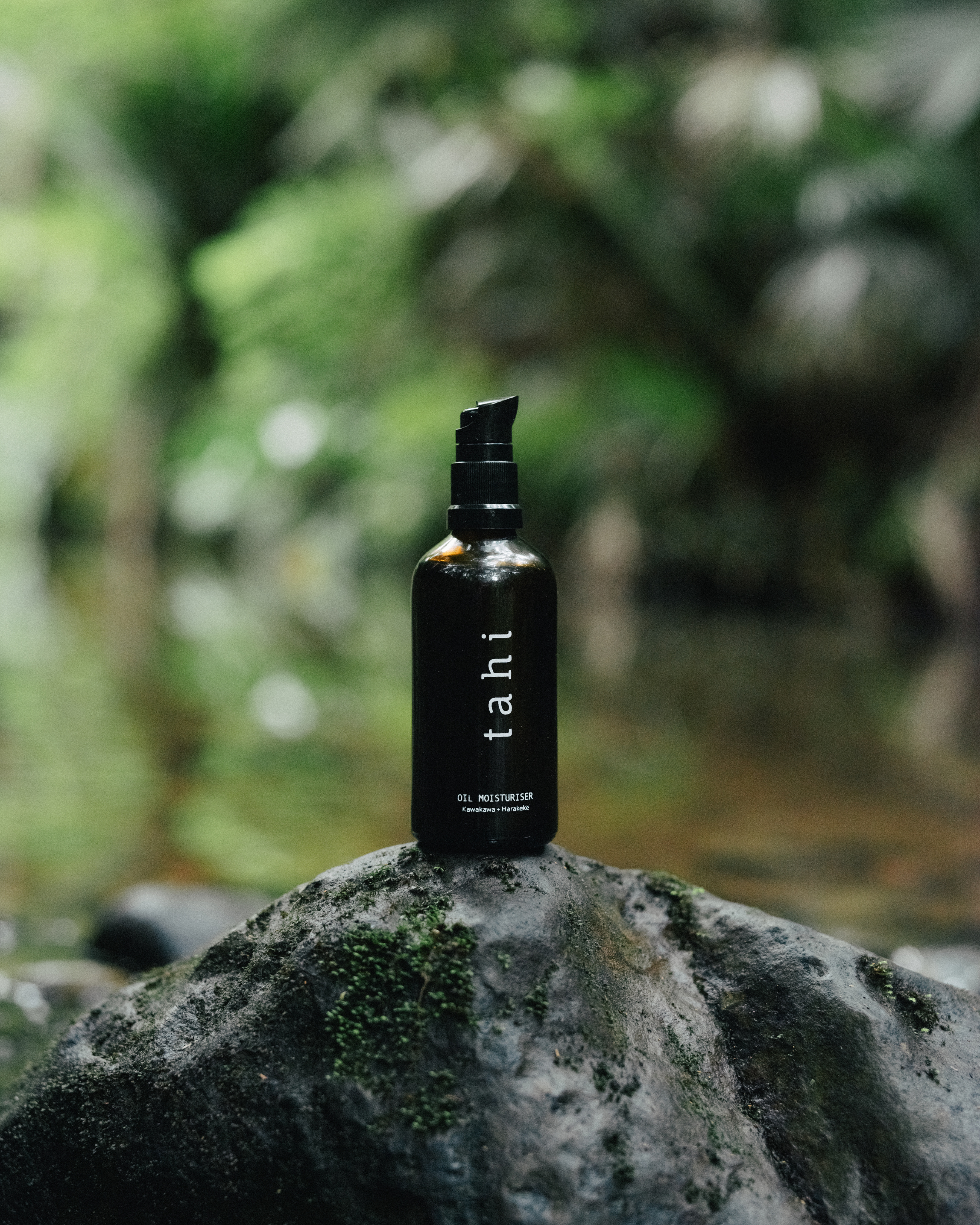 Black bottle labeled 'tahi' on a rock with a blurred natural background