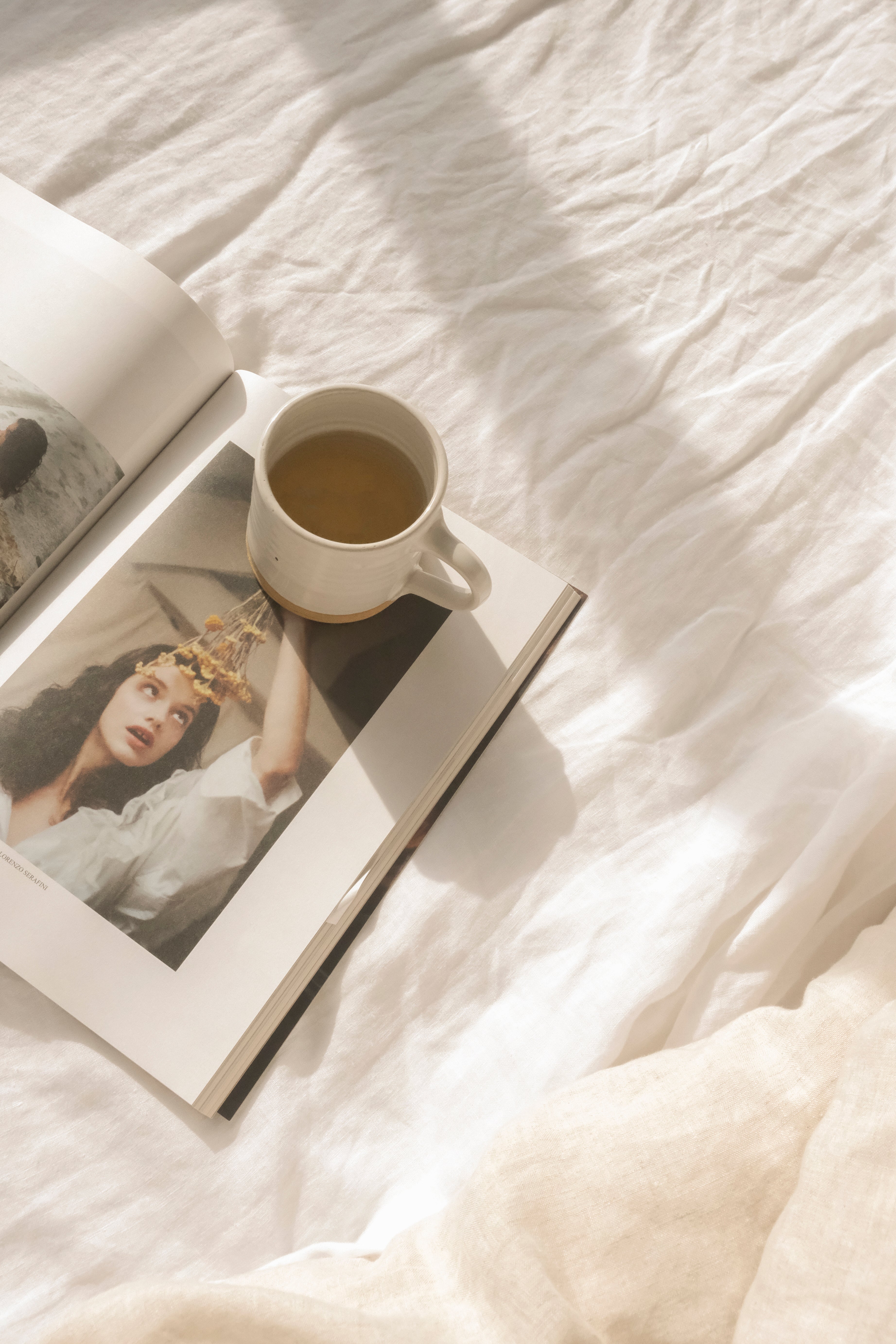 cup of tea sitting on a book on white linen bed sheets