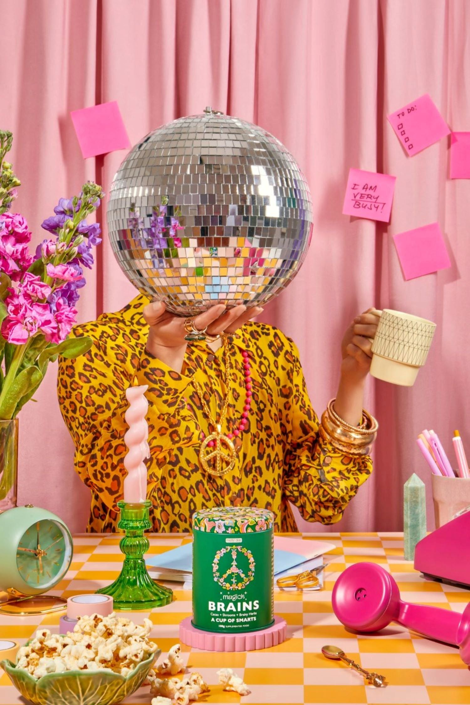 Person holding a disco ball with a pink curtain background, featuring a can of 'Brains' and decorative items.