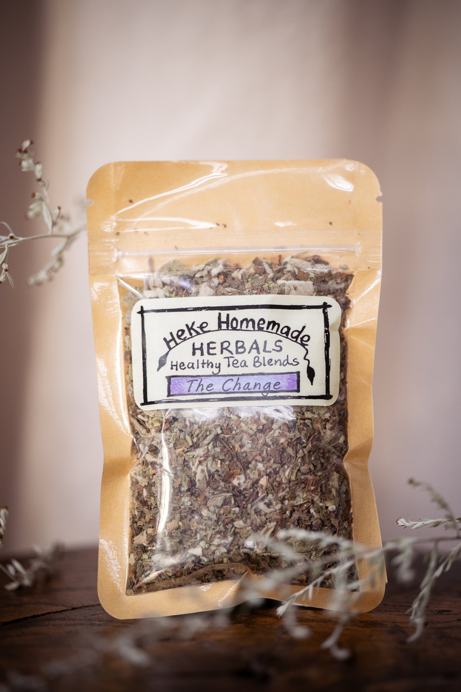 Packaged tea blend labeled 'Heke Herbals - The Change Tea' with visible herbs through the clear plastic front.