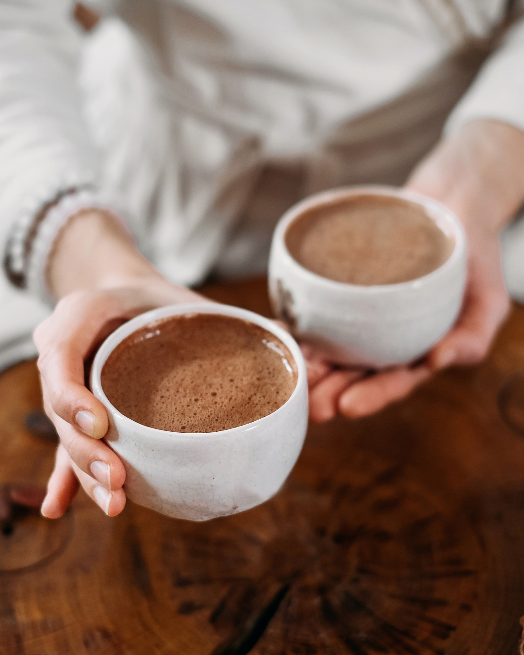 two hands holding two mugs of cacao