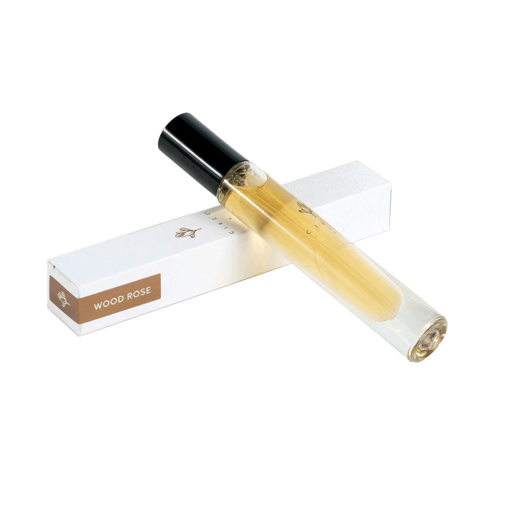 A small, clear glass bottle of Circe Natural Perfume with a label reading 'Wood Rose', alongside a white box with the product name.