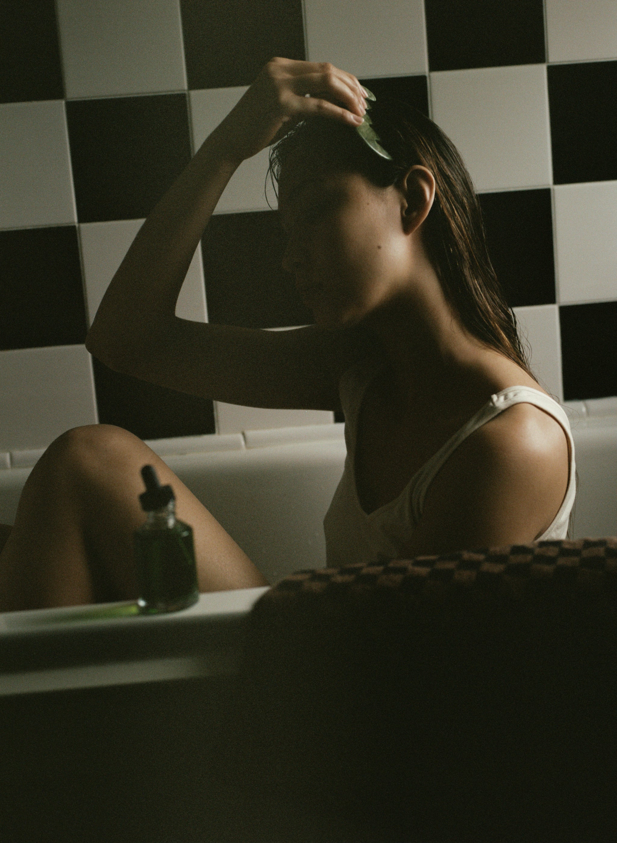 Woman sitting in a bathtub with a checkered wall behind her using HINU hair growth oil