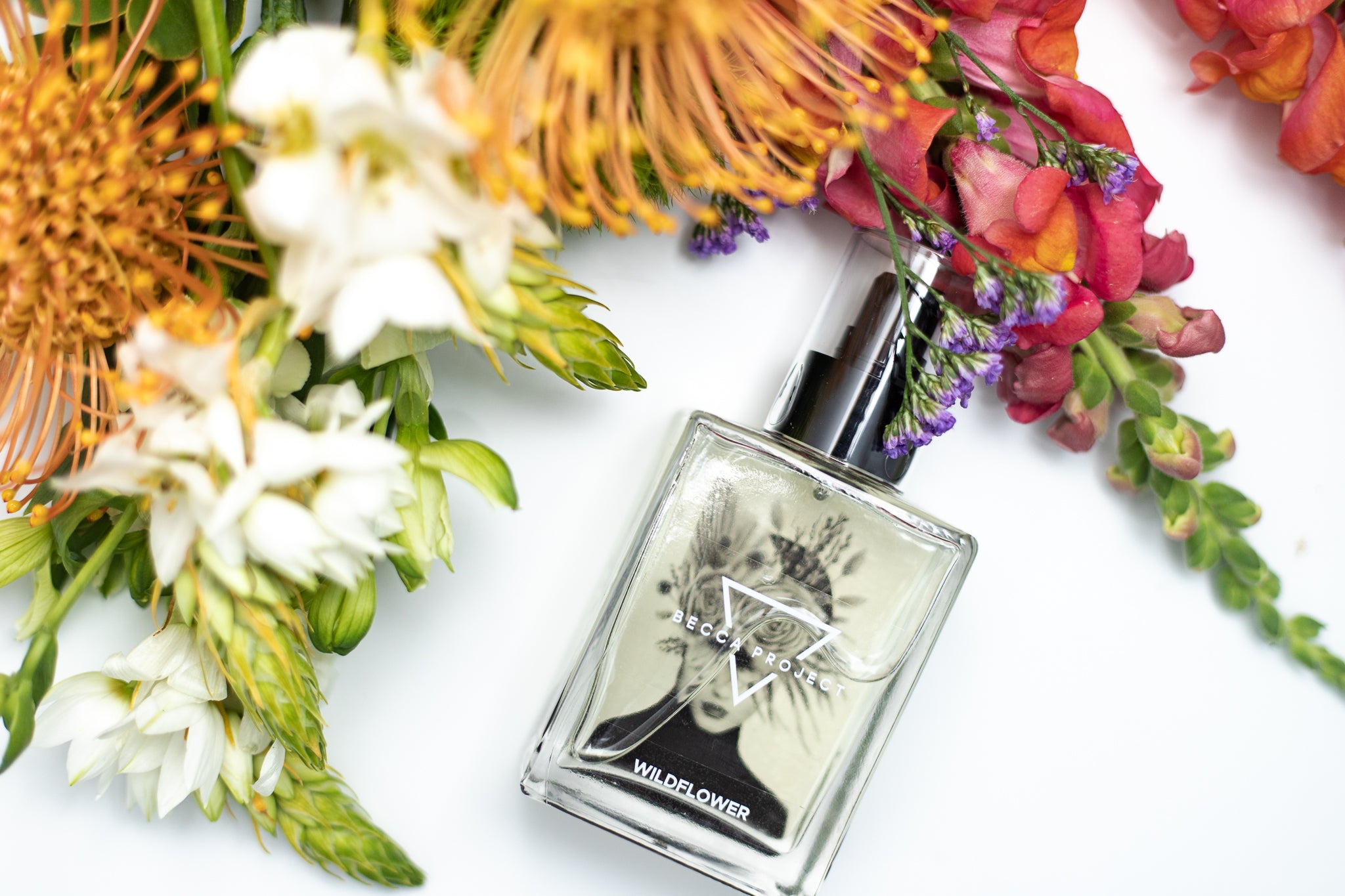Becca Project wildflower body oil in a flat lay with fresh flowers