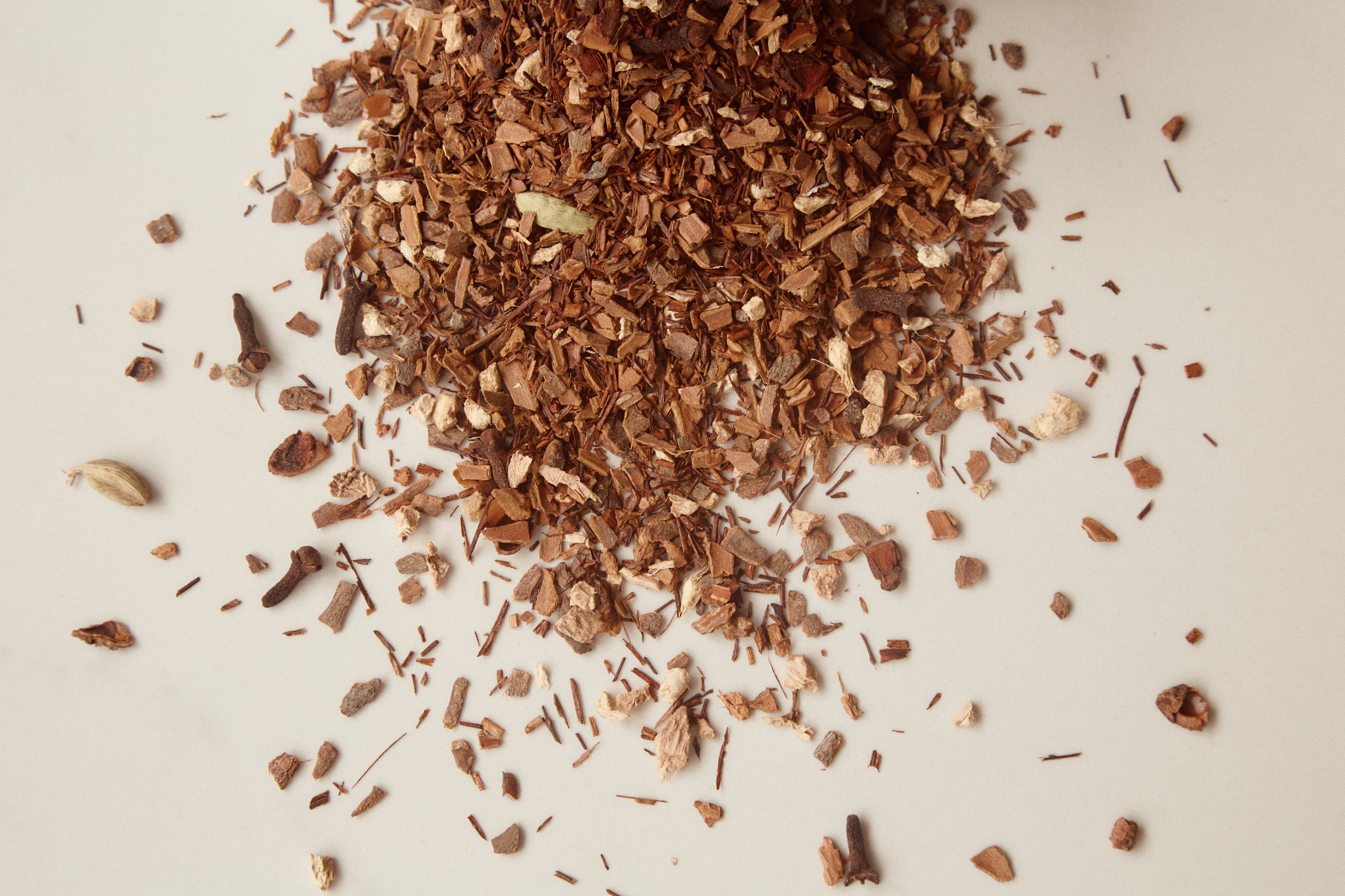 A scattered pile of dried herbal tea leaves and pieces, including rosehips and potential elderberries, on a light background.