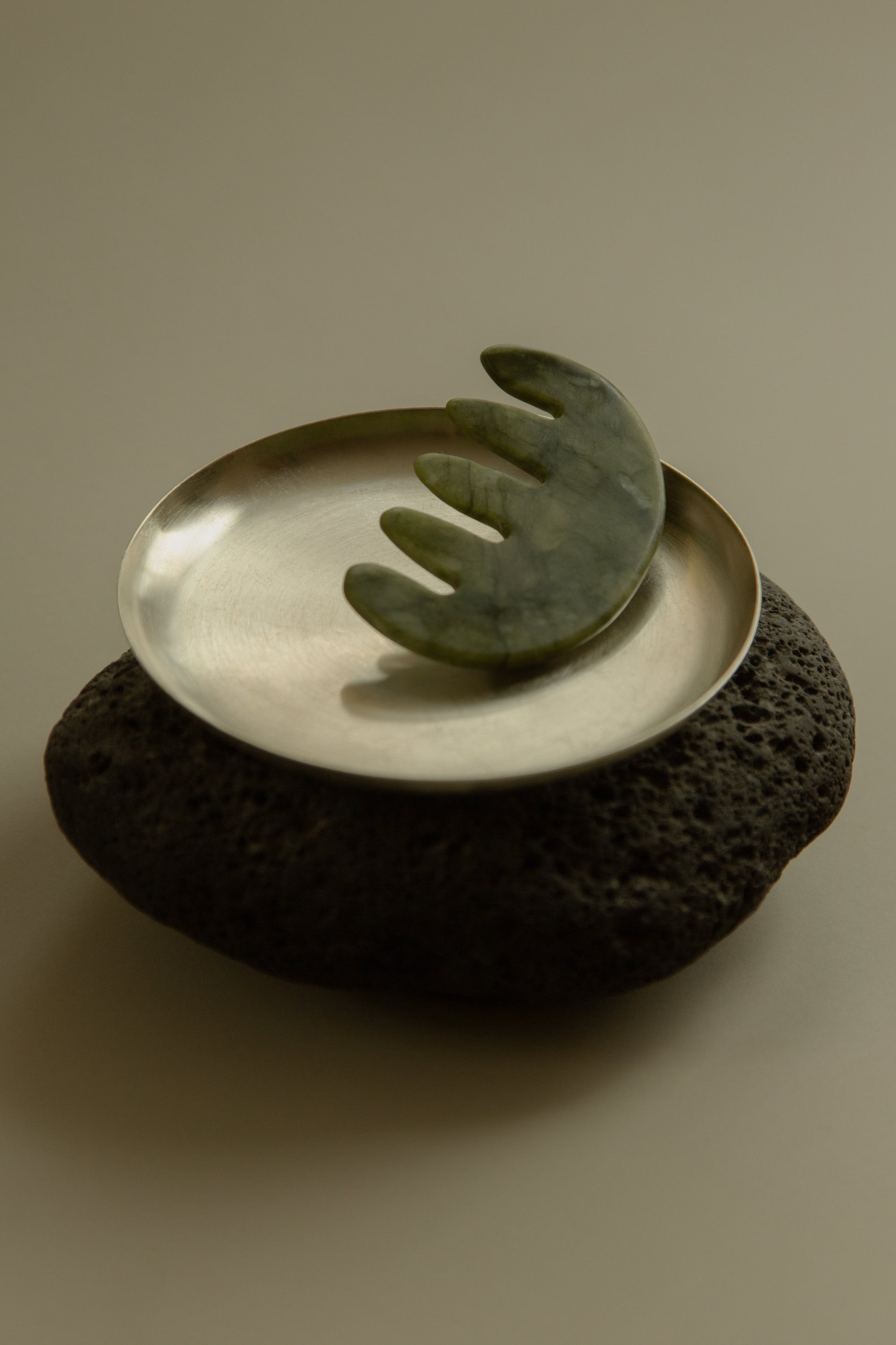 HINU Jade scalp stimulator resting on a metal tray on a dark rock