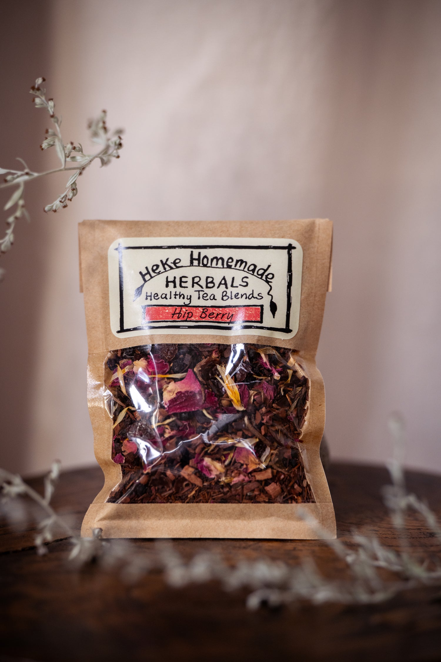 Packaged Hip Berry Tea by Heke Herbals, showing the product through a clear window with a brown paper wrap. The tea appears as a blend of dried fruits and herbs.