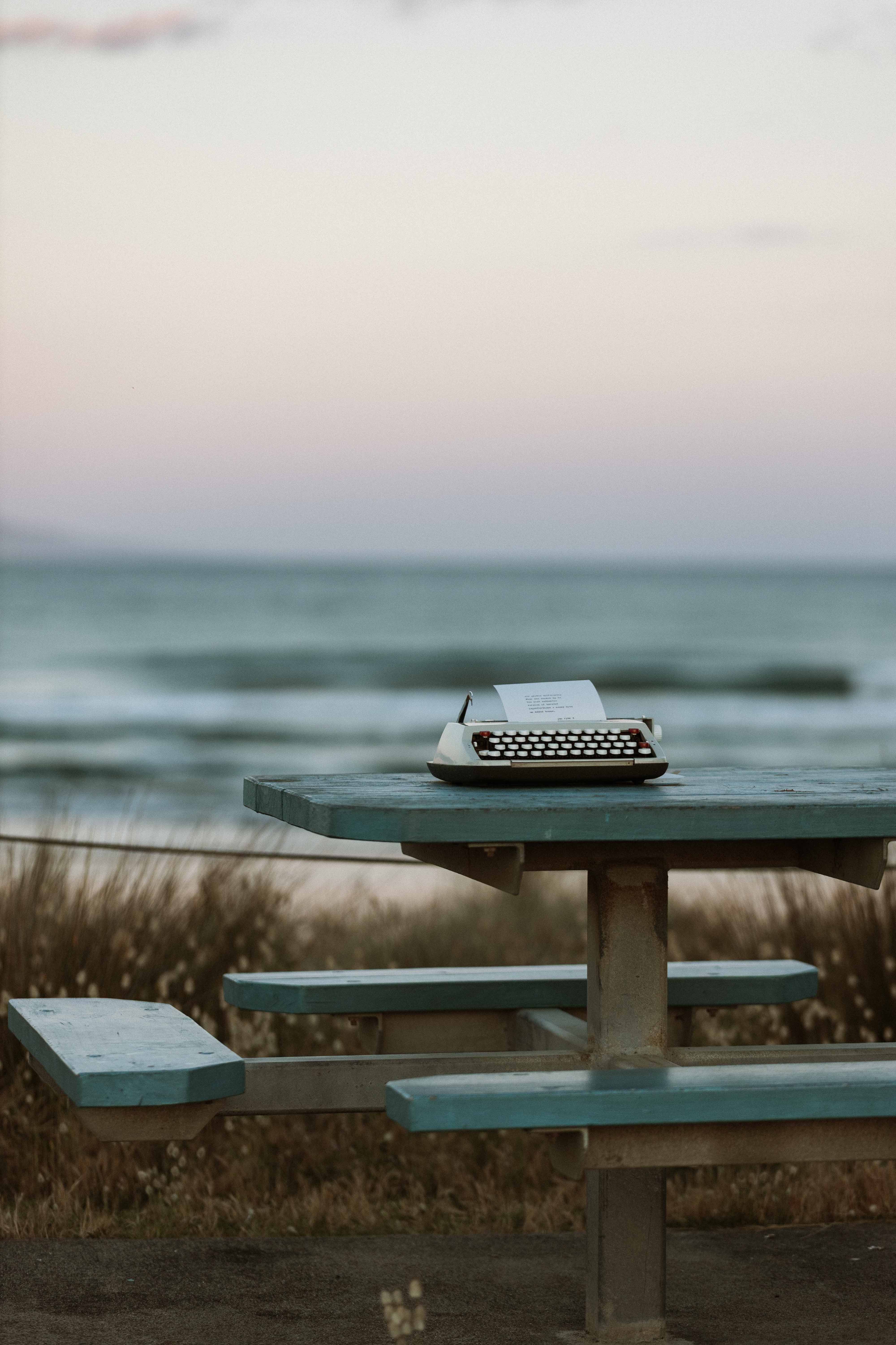 Vintage typewriter on a wooden bench by the ocean at sunset