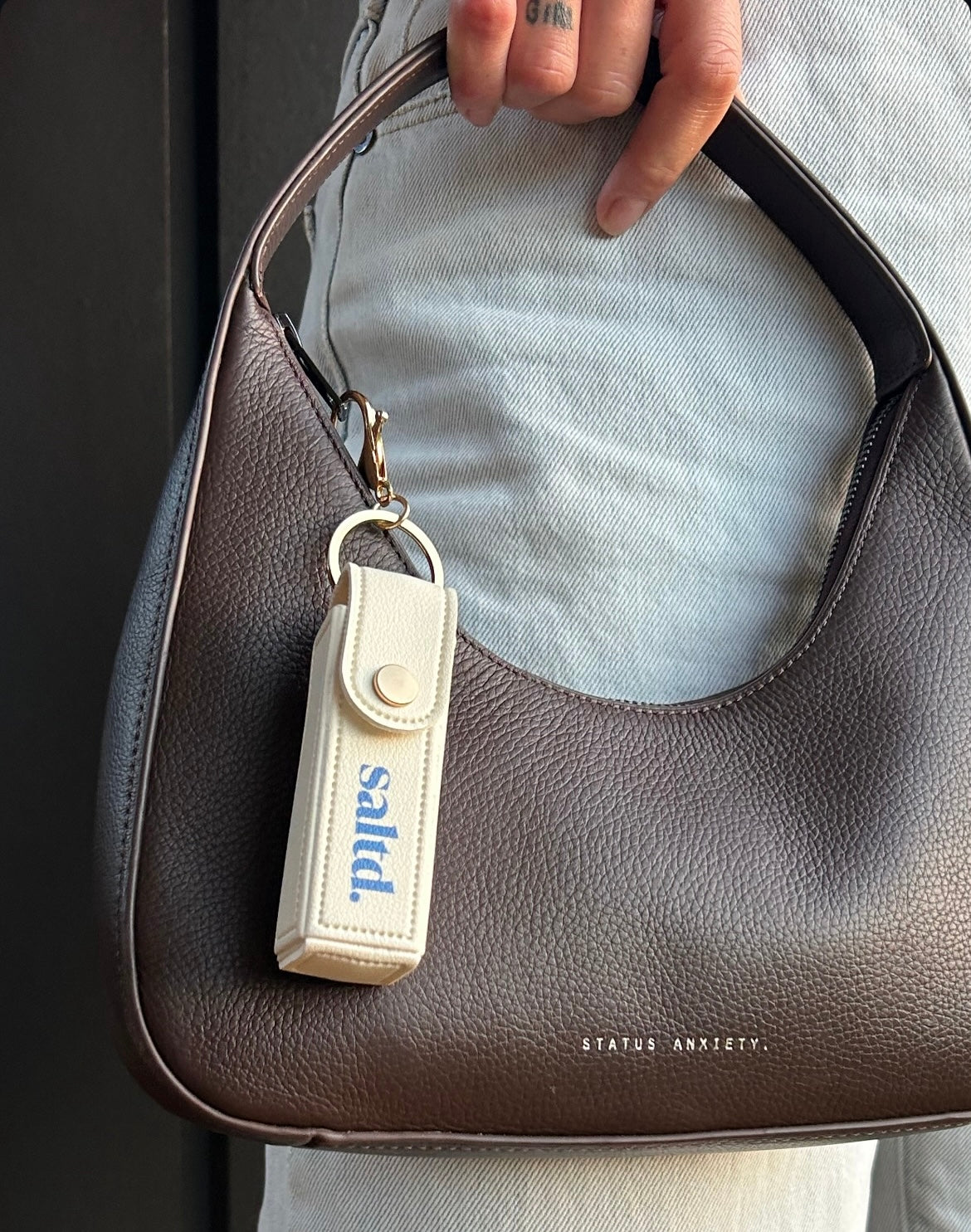 Keychain with 'sadly' text attached to a brown leather handbag.