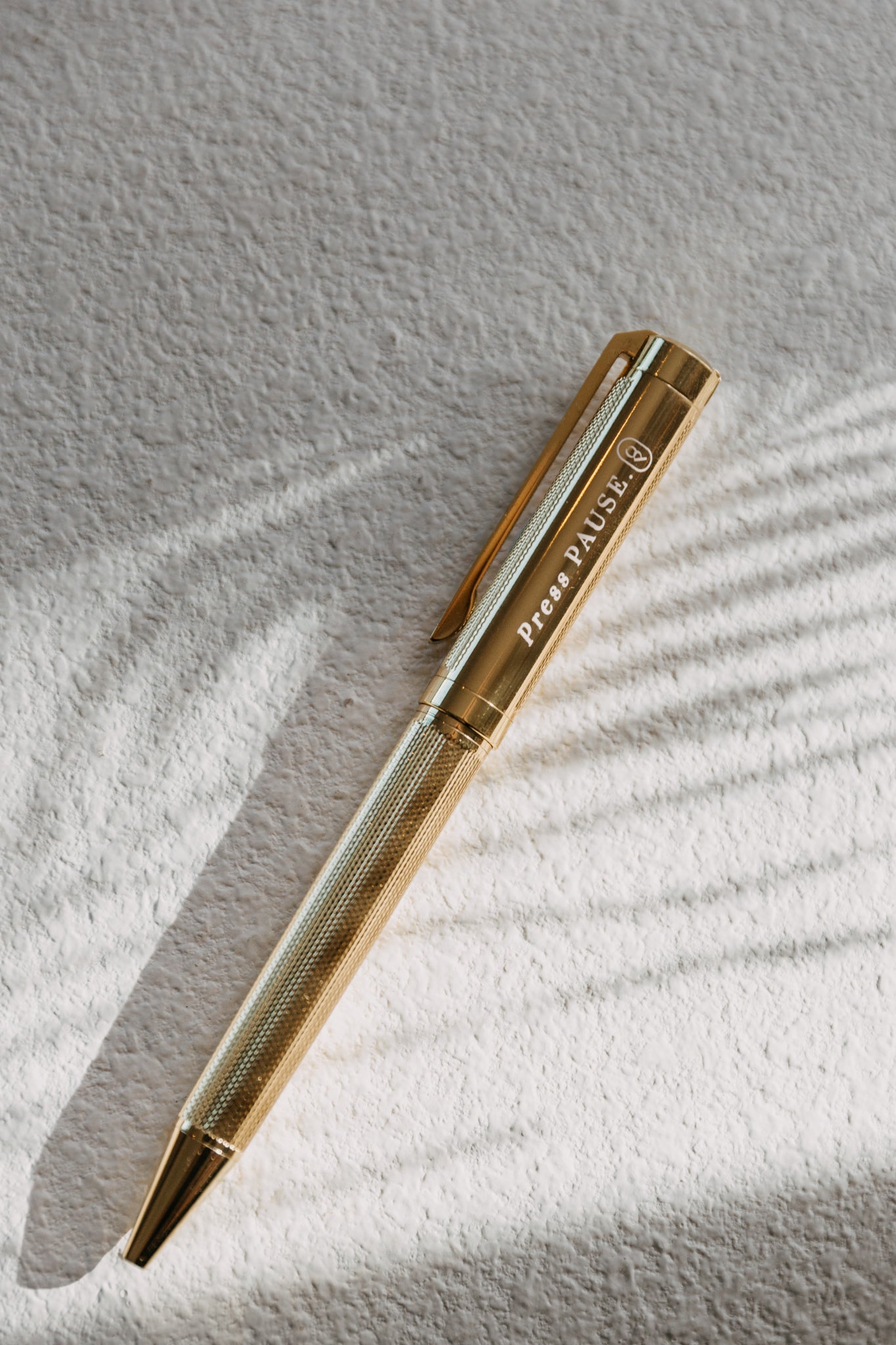 Olive and Page gold 'press pause' pen resting on textured paper