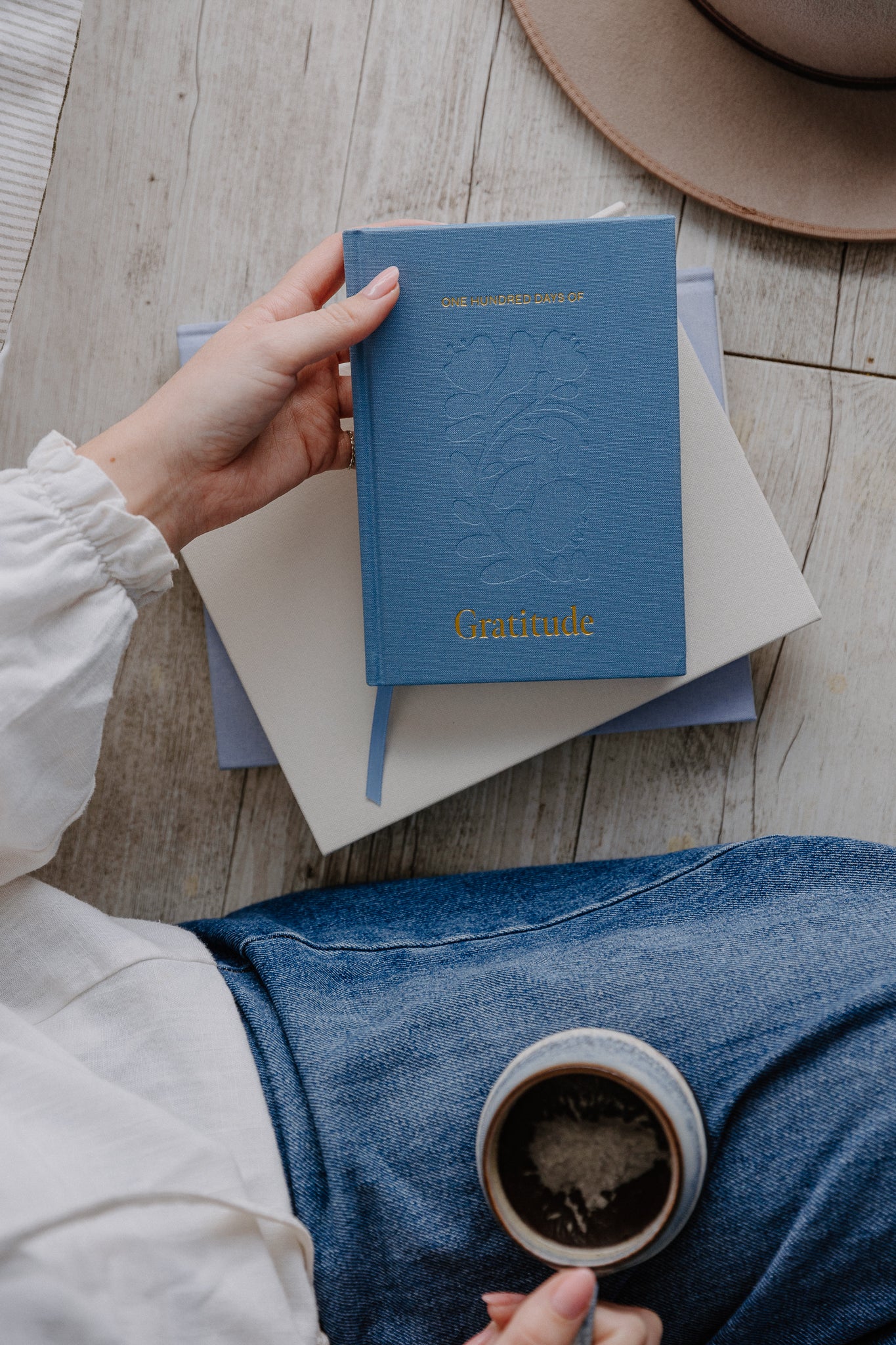 woman holding a blue gratitude journal while holding a cup coffee