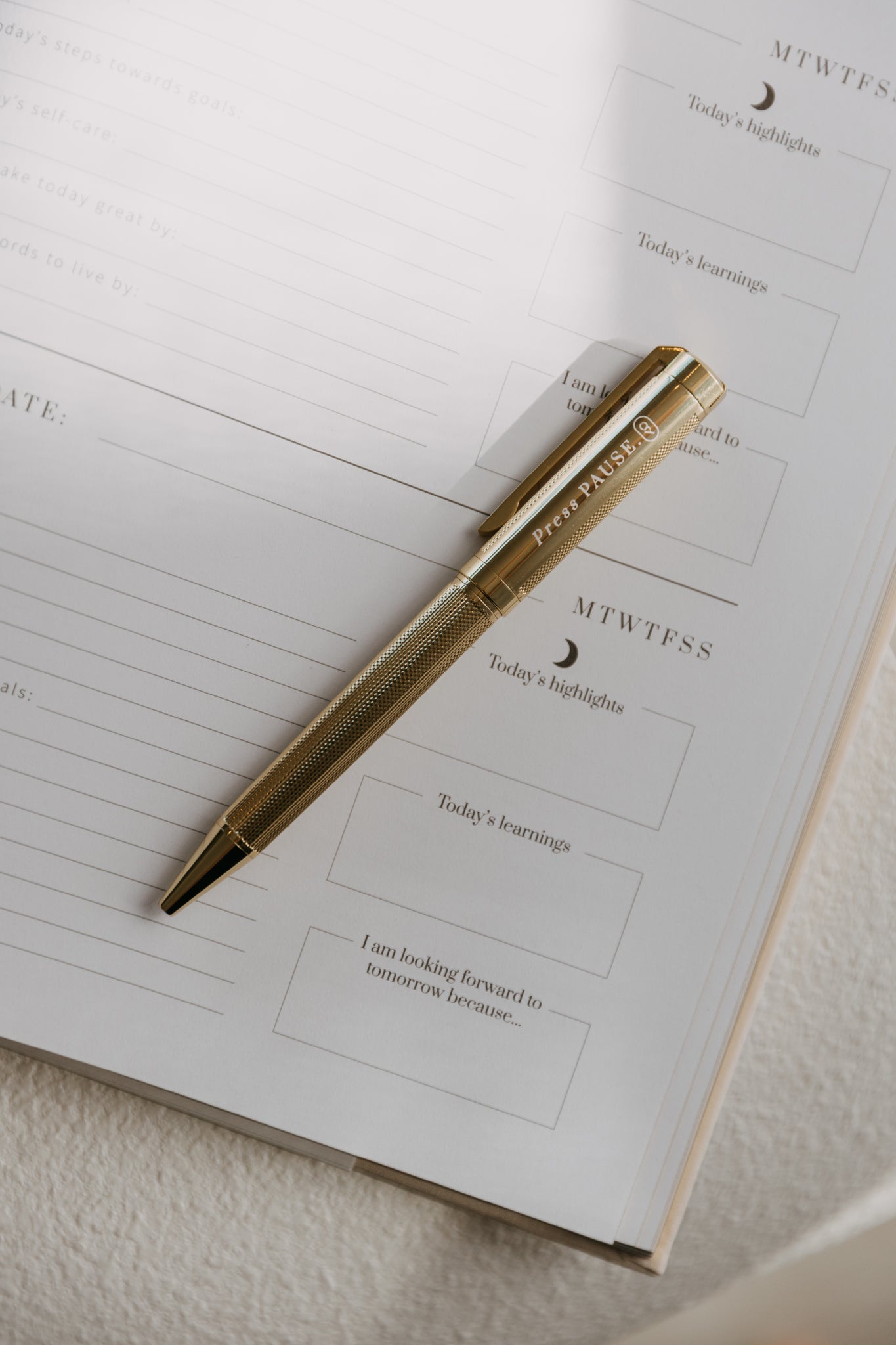 Olive and Page gold 'press pause' pen resting on a journal