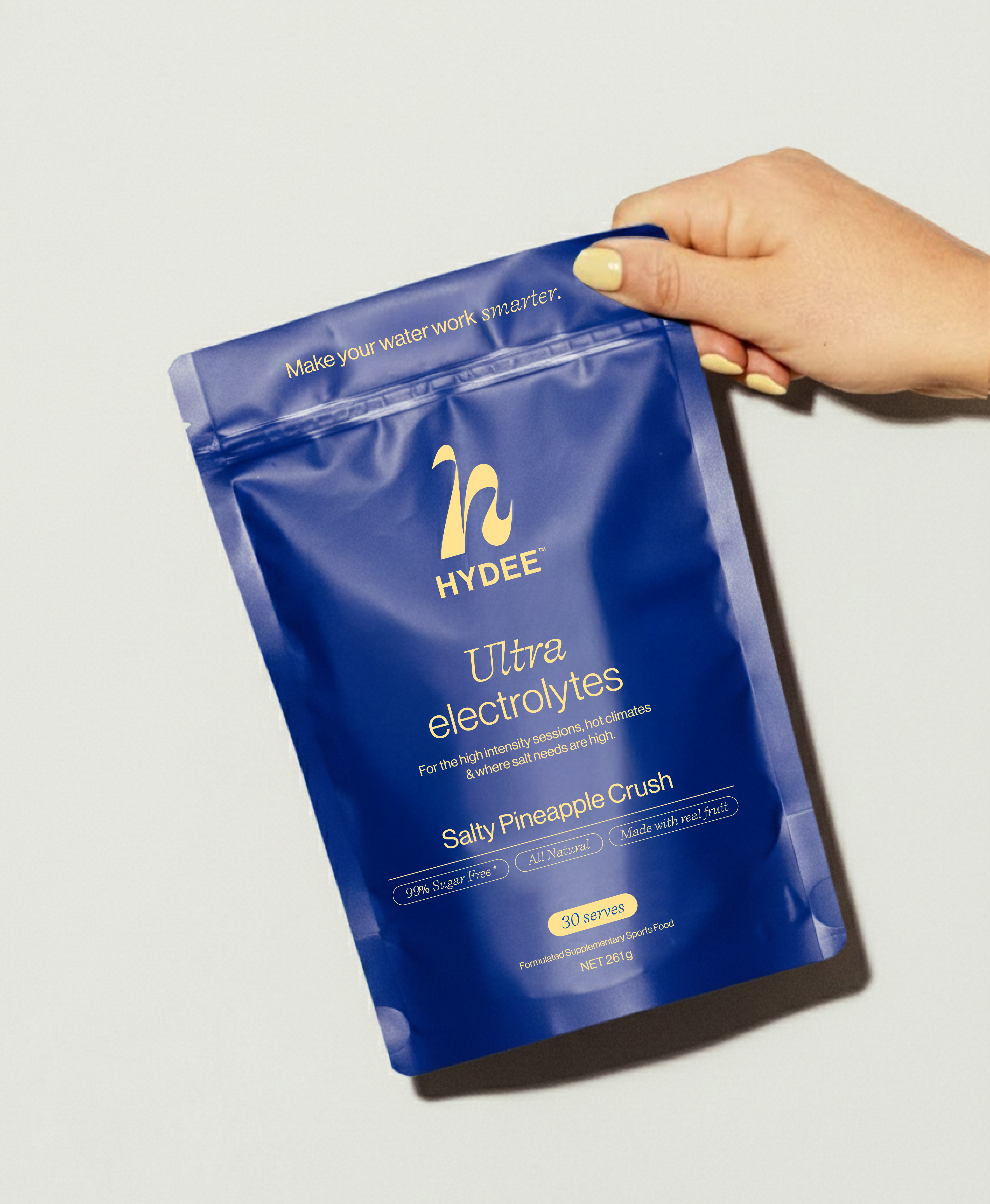 Hand holding a blue Hydee Ultra Electrolytes packet on a light gray background