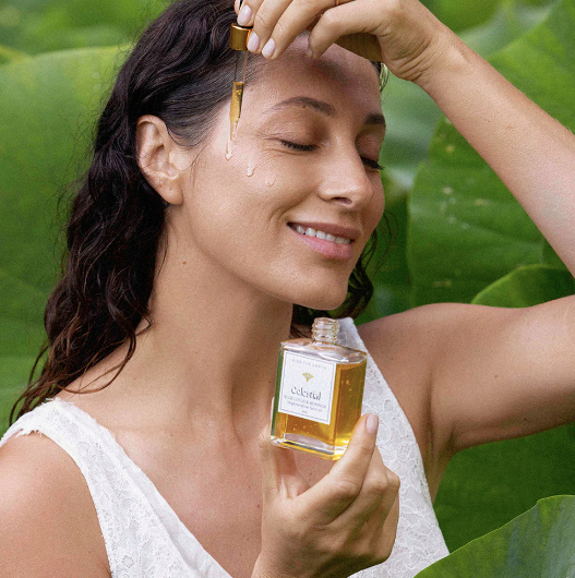 A woman applying Kiss the Earth Celestial face oil onto her face