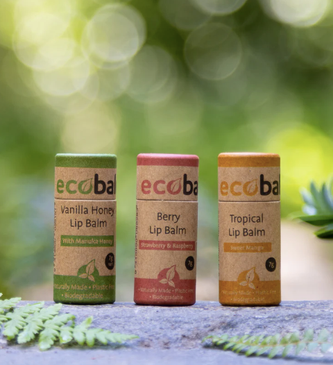Three Ecobalm lip balms with green, pink, and orange packaging on a natural background.