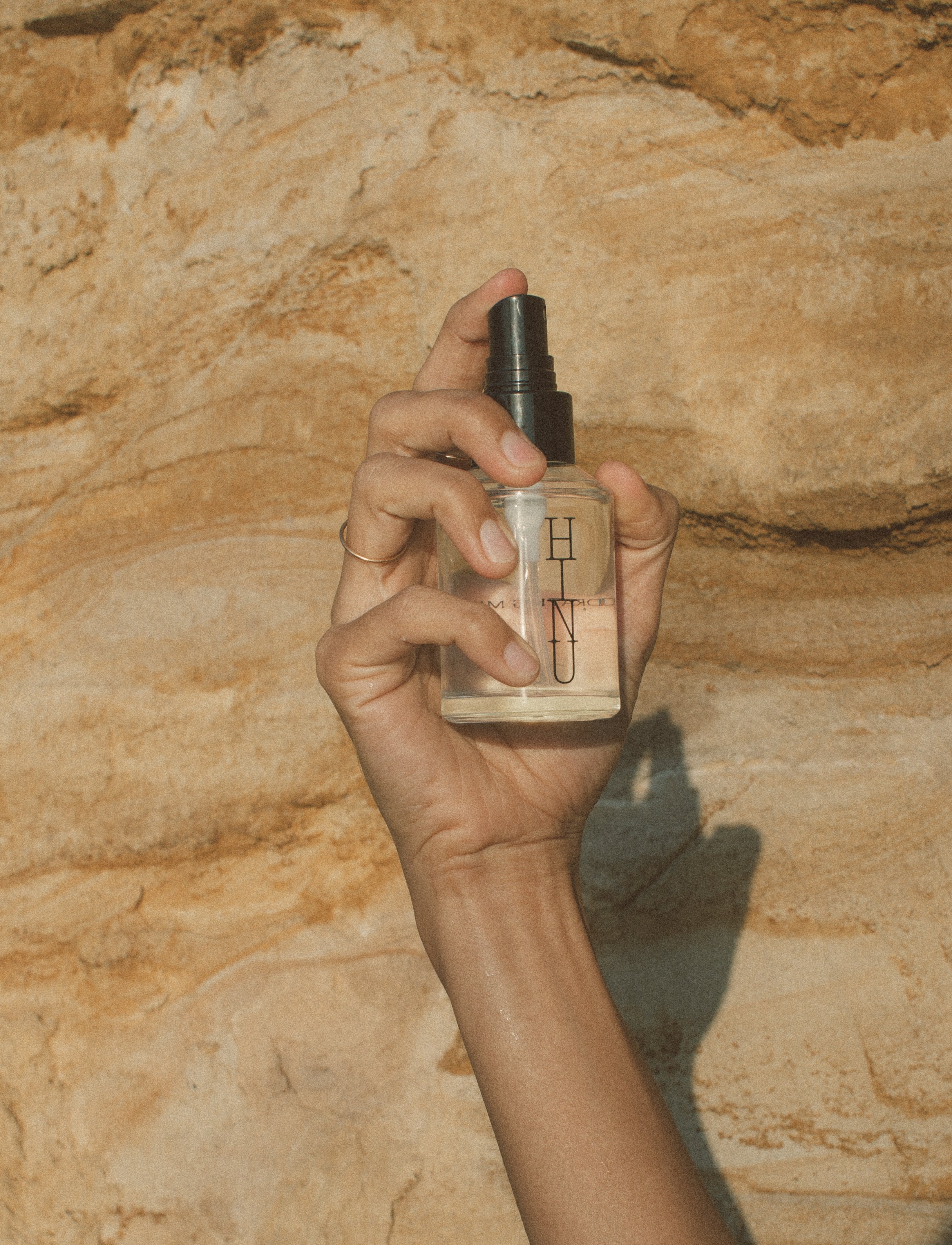 Hand holding a bottle of HINU hydrating hair spray against a stone wall background